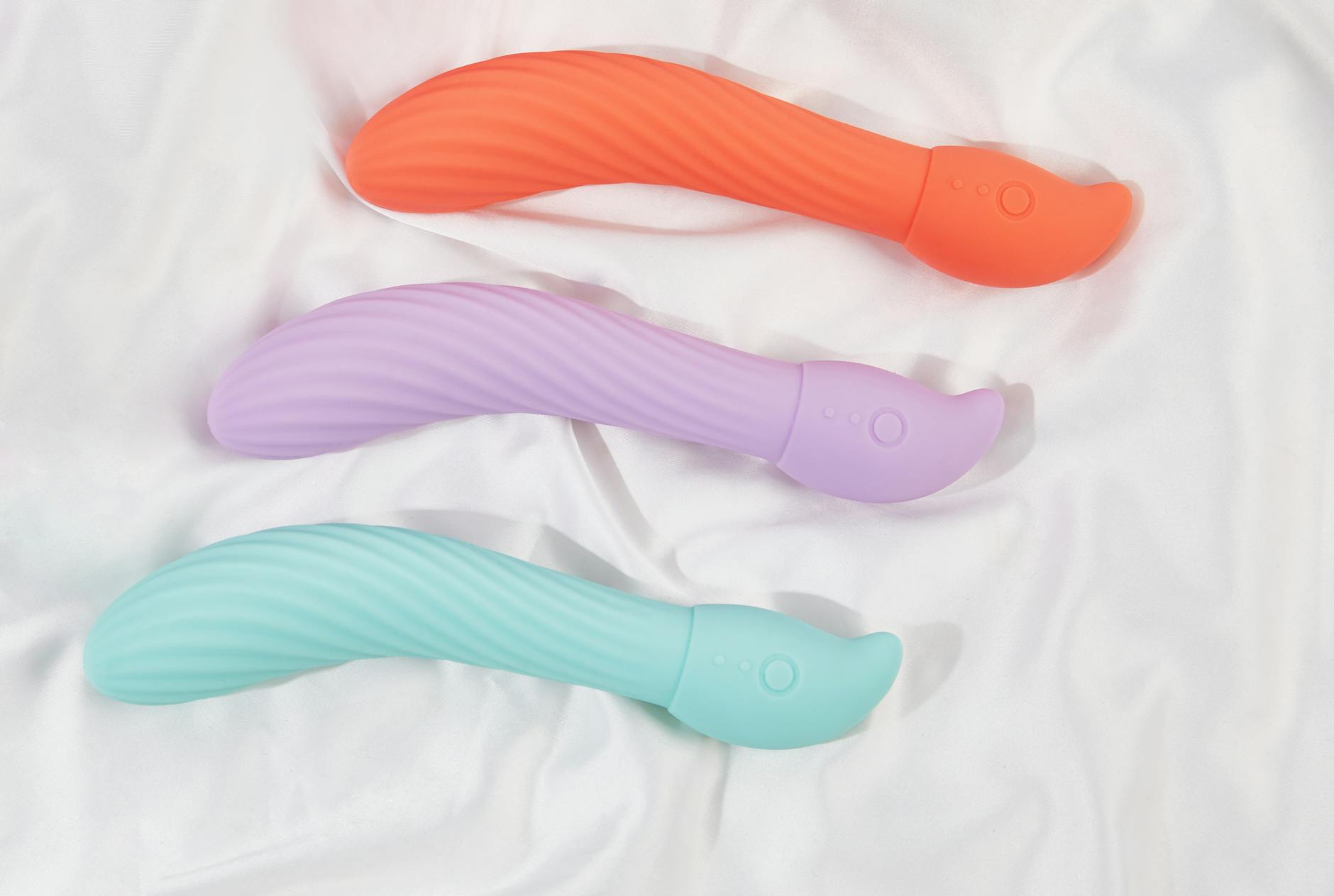 Three colorful vibrators arranged on white fabric highlighting smooth silicone texture