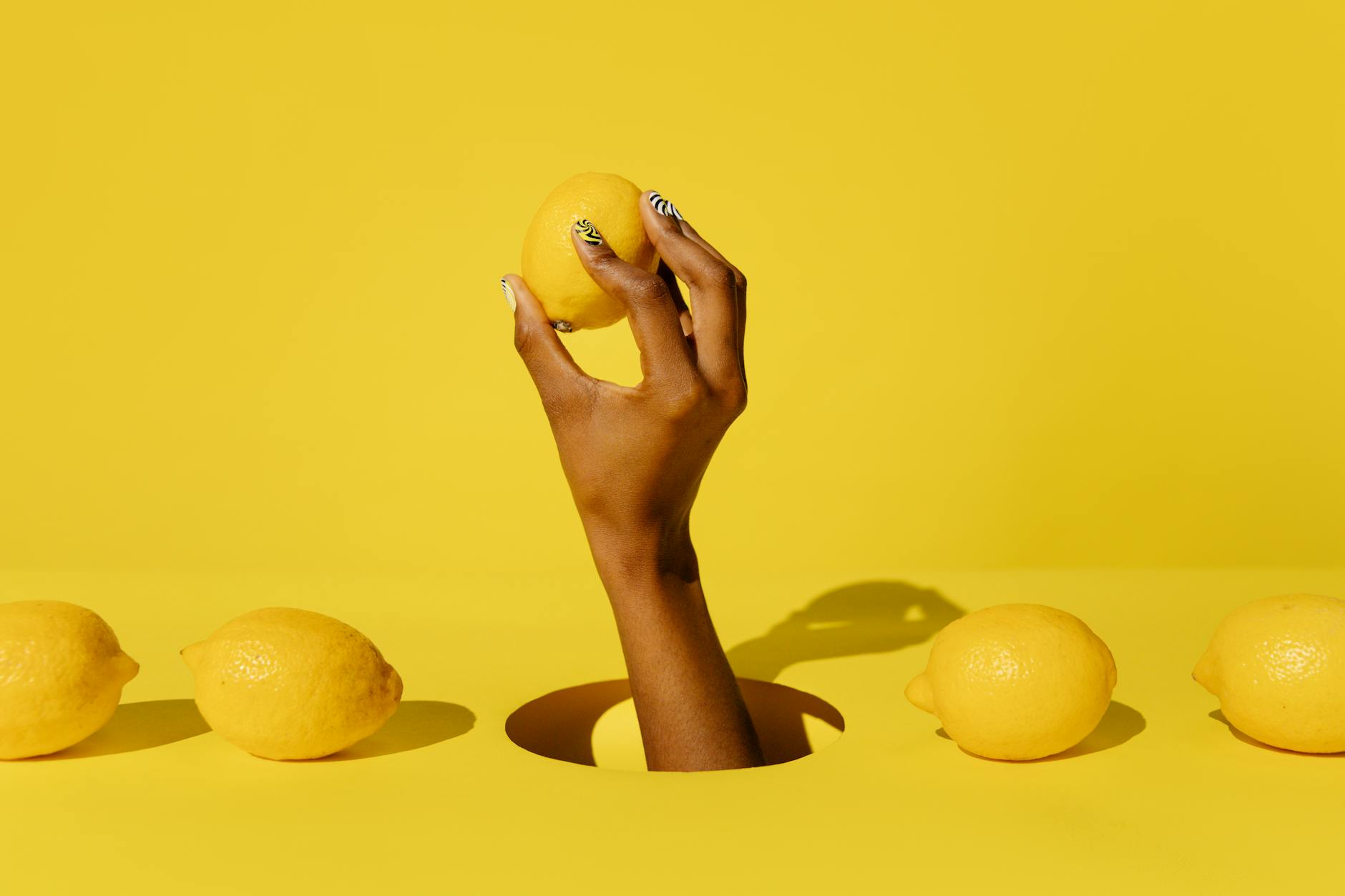 Hand holding a fresh lemon against a bright yellow background, symbolizing the slow-release warmth of extended pleasure