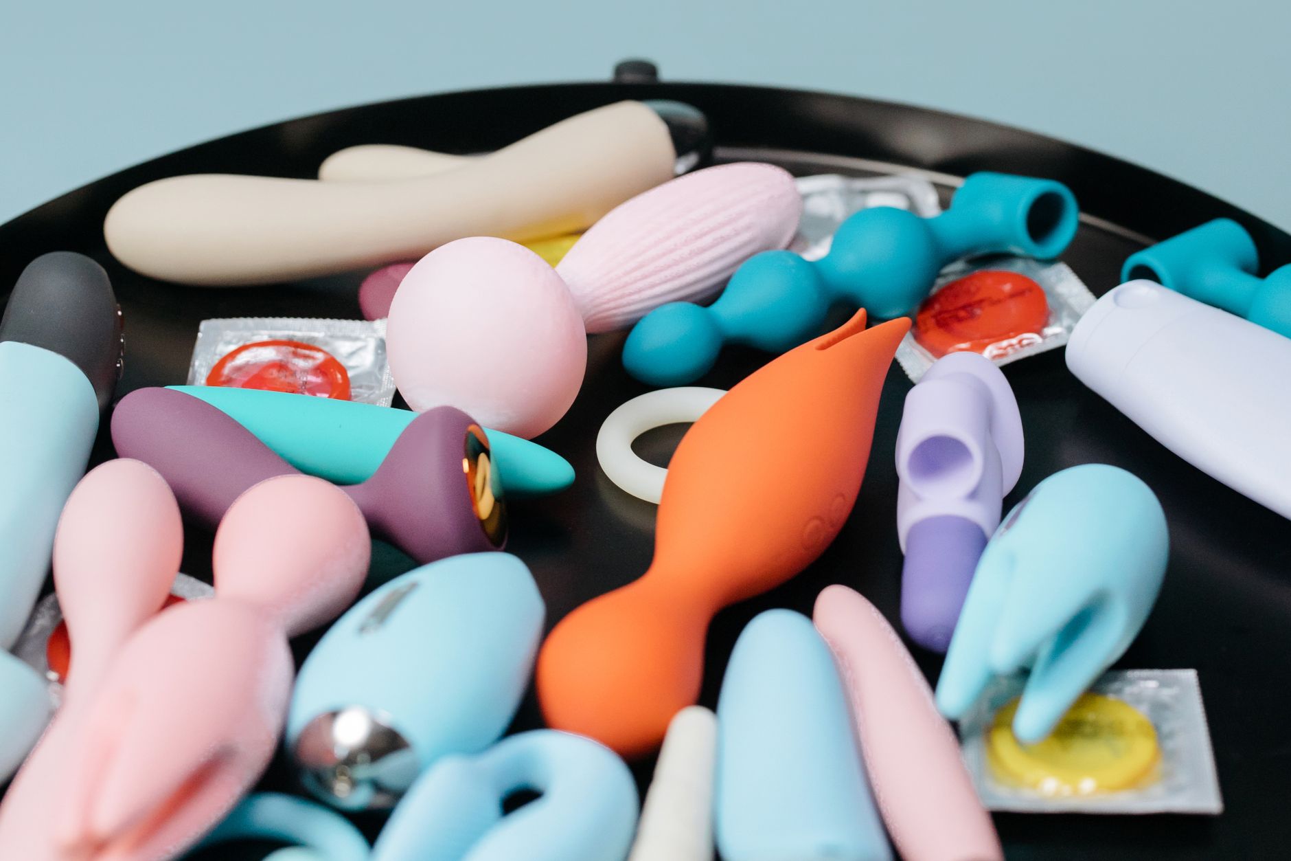 Woman holding blue and pink silicone vibrators in a thoughtful pose
