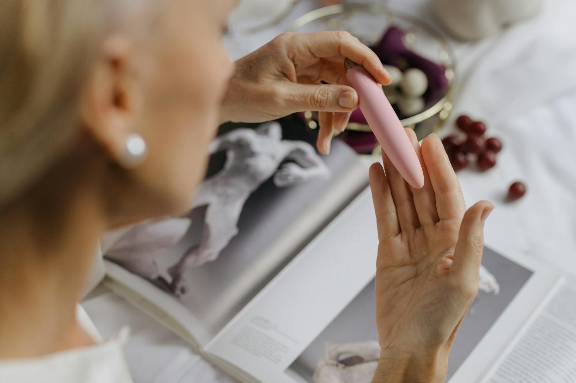 A woman holding a pink vibrator with books in the background, representing intimate exploration