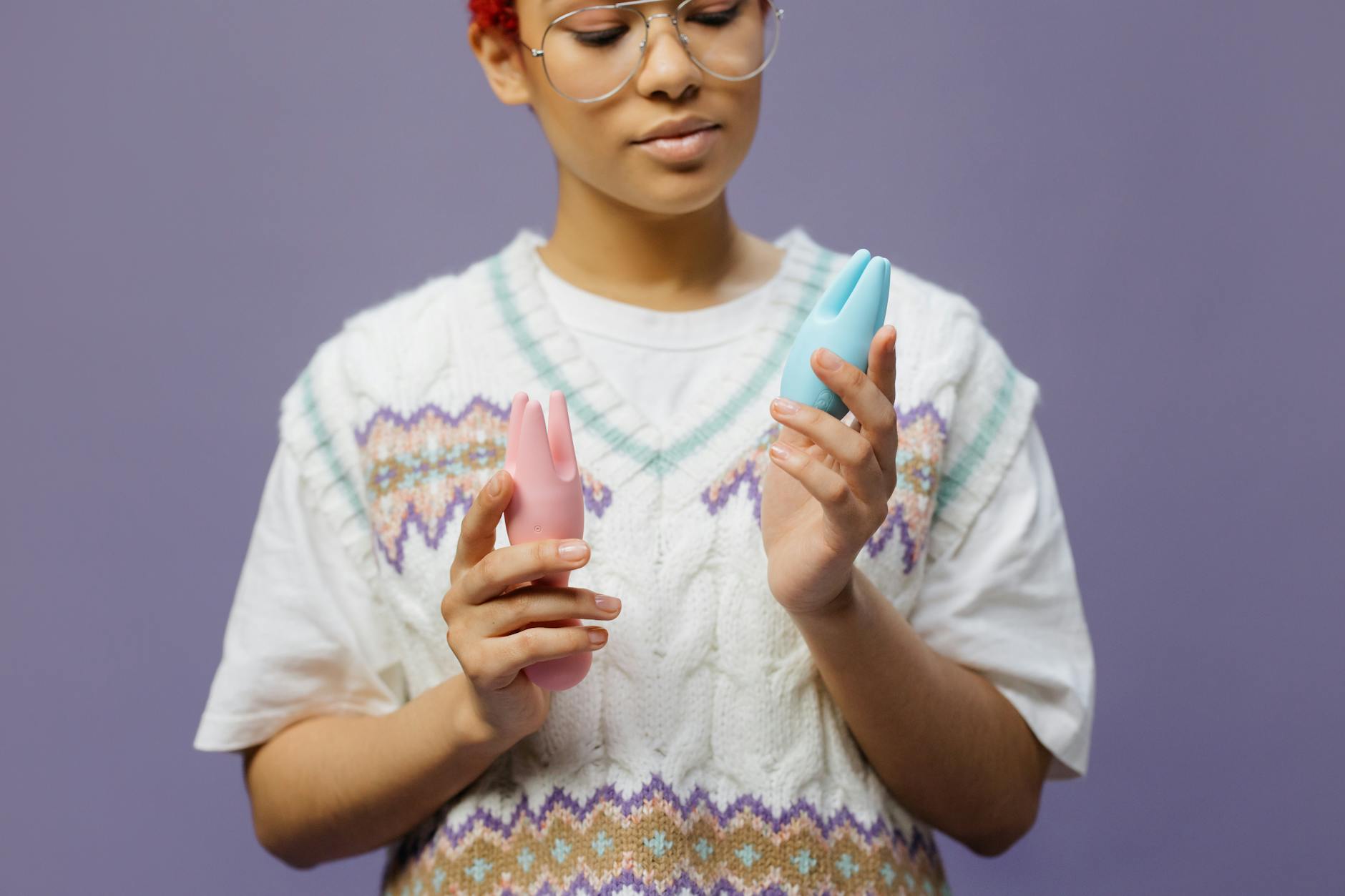 Person holding blue and pink silicone vibrators in a contemplative moment of self-exploration.