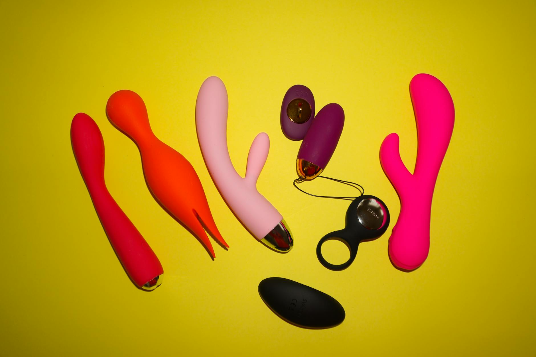 Colorful silicone sex toys arranged on bright yellow background showcasing modern pleasure devices