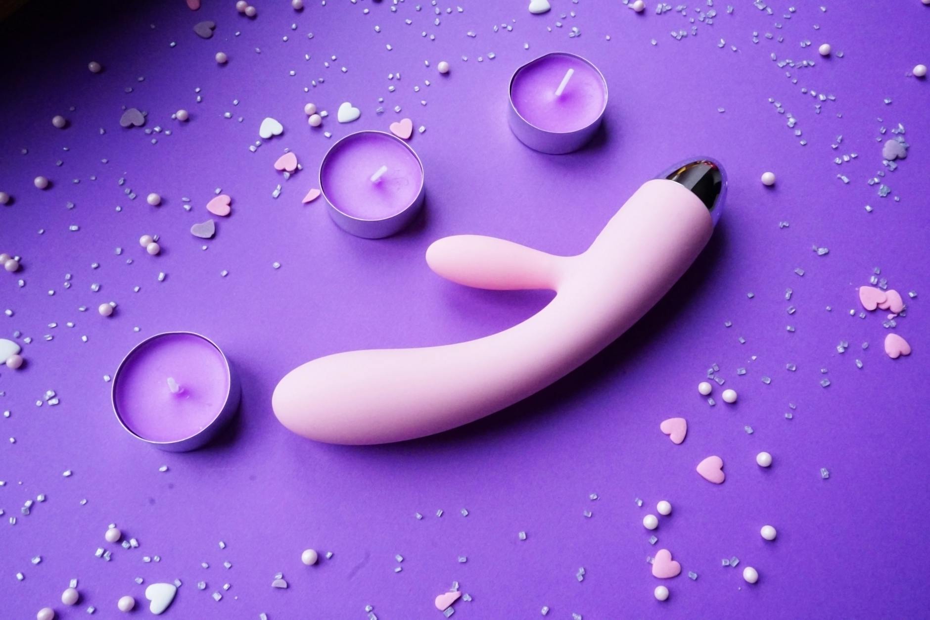 Intimate moment with a pink vibrator, heart confetti, and candles on a romantic surface
