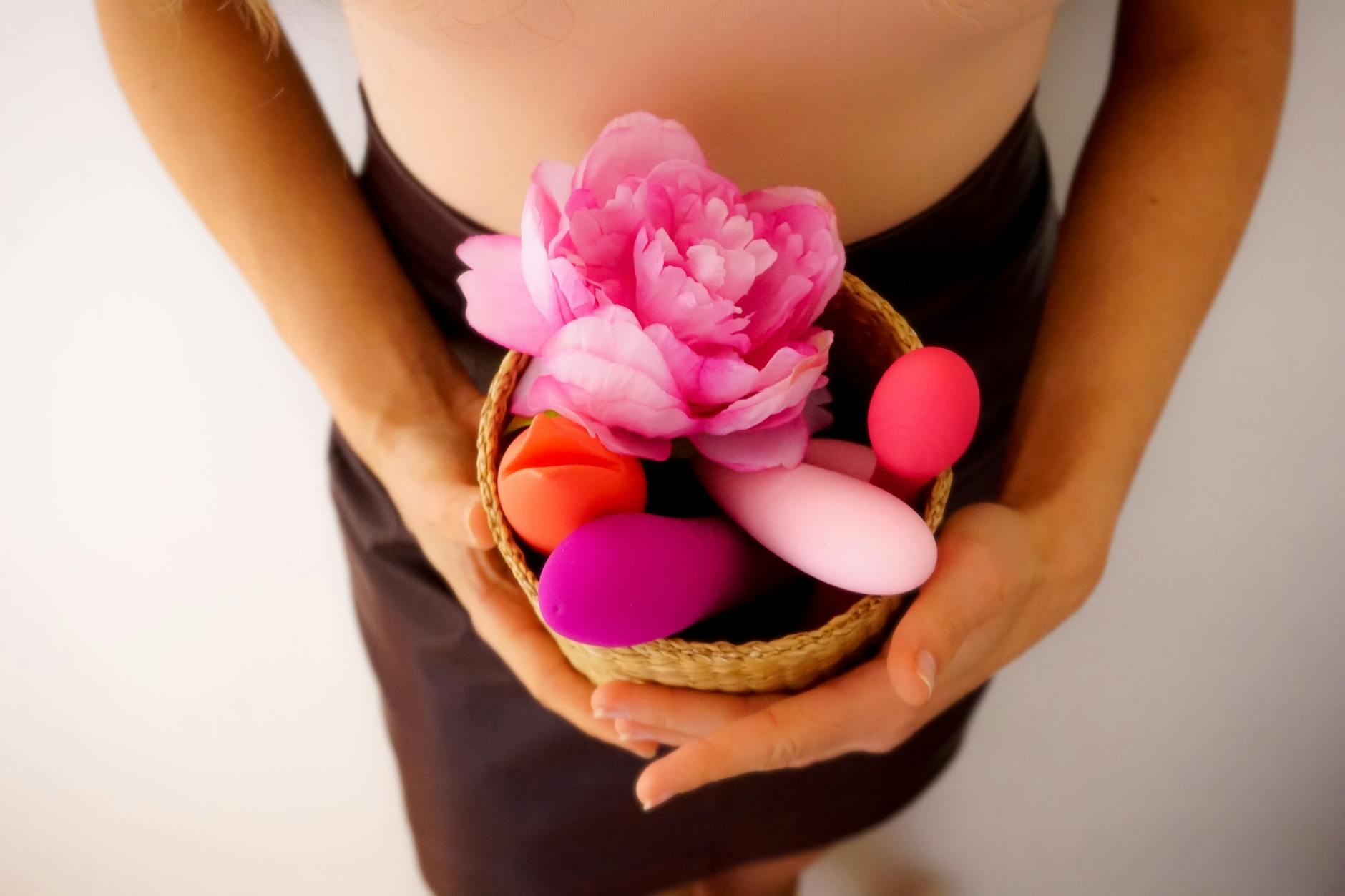 Cesta contendo vibradores coloridos e flor rosa, simbolizando diversidade de brinquedos para adultos